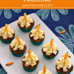 Mini carrot cake cupcakes topped with cream cheese frosting and fondant carrots on a serving plate.