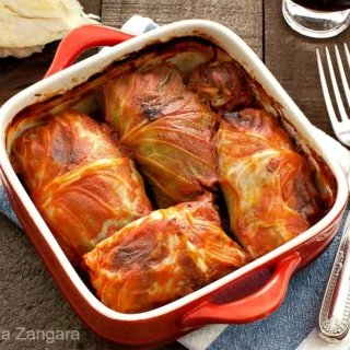 Baked cabbage rolls in tomato sauce served in a red baking dish.