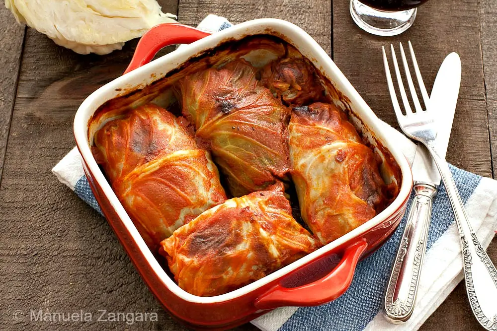 Baked cabbage rolls in tomato sauce served in a red baking dish.