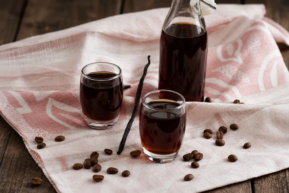 Coffee and Vanilla Liqueur served in small glasses beside a glass bottle with coffee beans and vanilla pods.