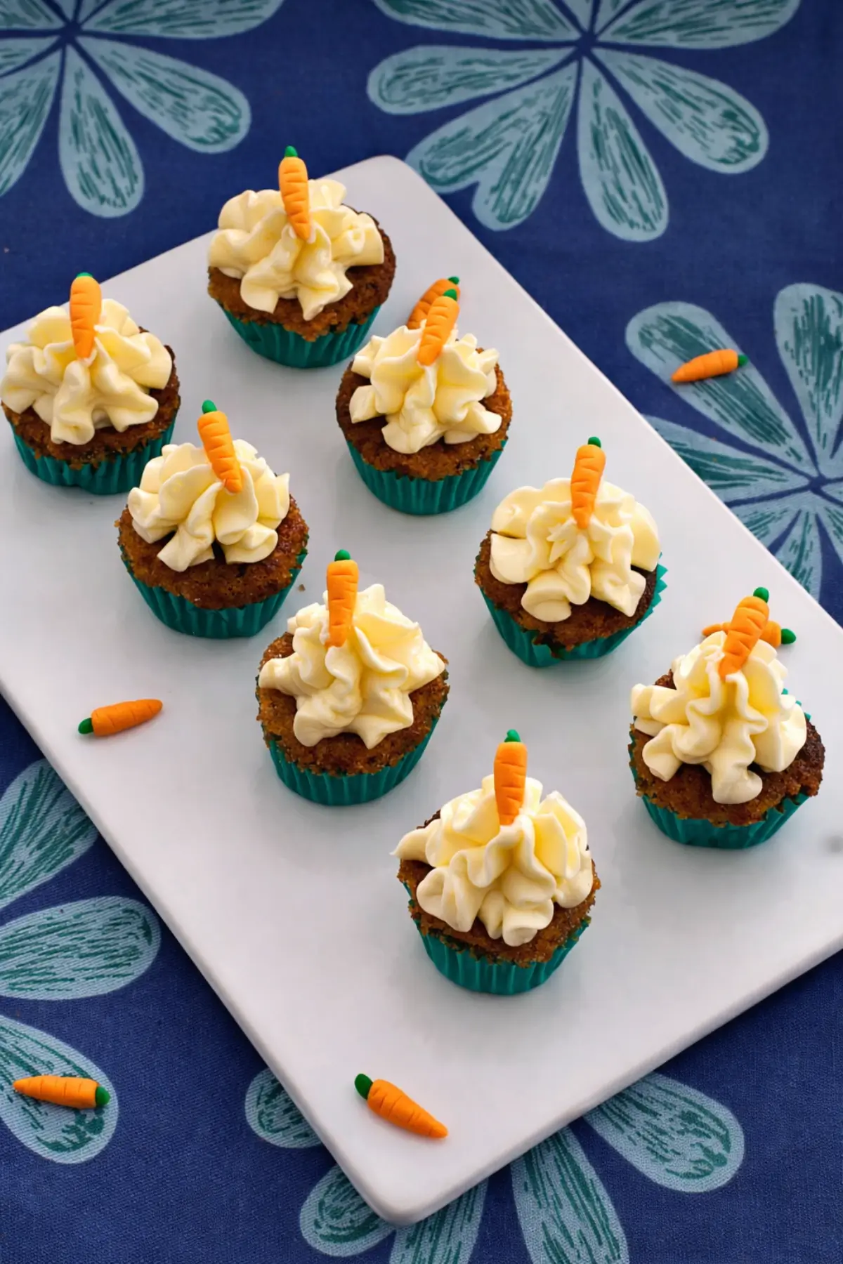 Mini carrot cake cupcakes topped with cream cheese frosting and fondant carrots on a serving plate.