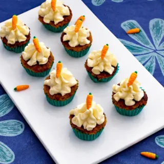 Mini carrot cakes with cream cheese frosting and fondant carrots served on a plate.