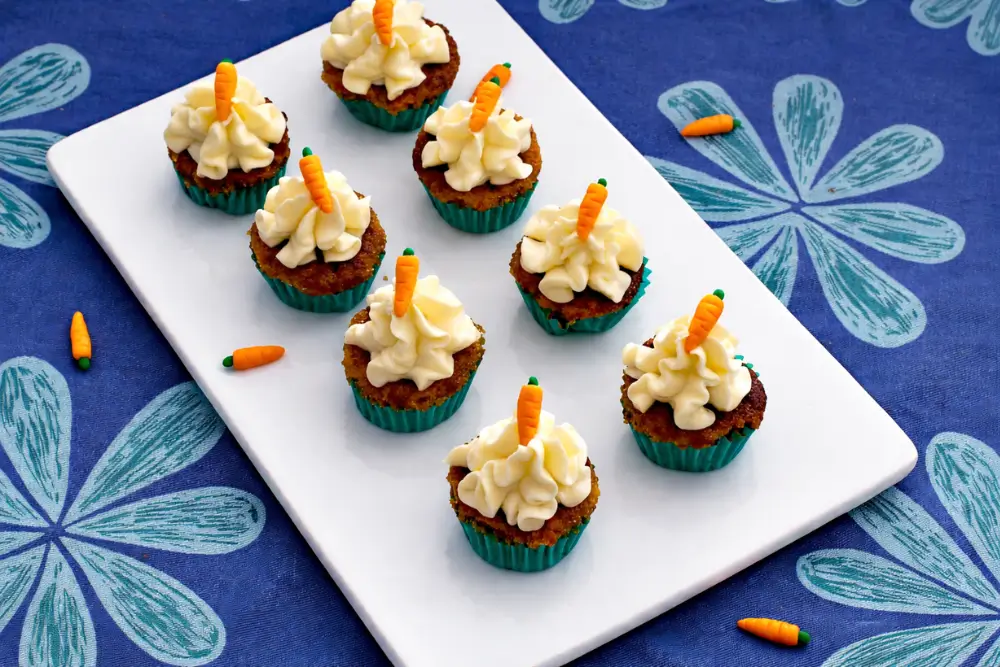 Mini carrot cakes with cream cheese frosting and fondant carrots served on a plate.
