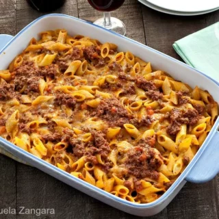 Baked Pasta al Forno topped with rich meat sauce and melted cheese in a white baking dish on a rustic wooden table.