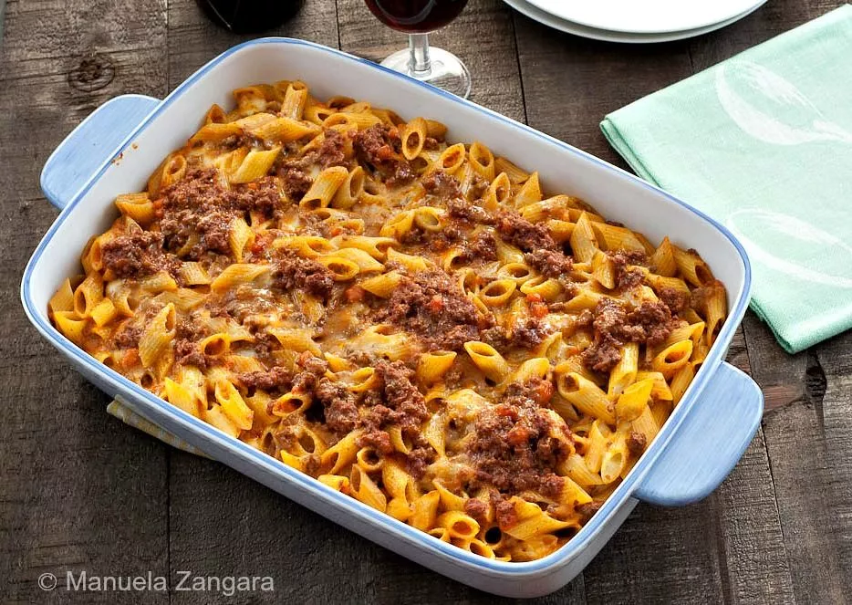 Baked Pasta al Forno topped with rich meat sauce and melted cheese in a white baking dish on a rustic wooden table.