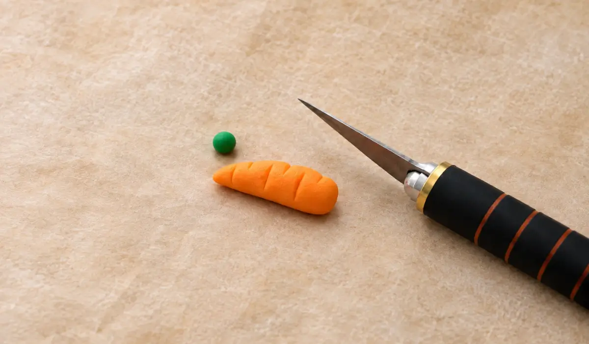 Orange fondant carrot beside a green fondant ball and craft knife.