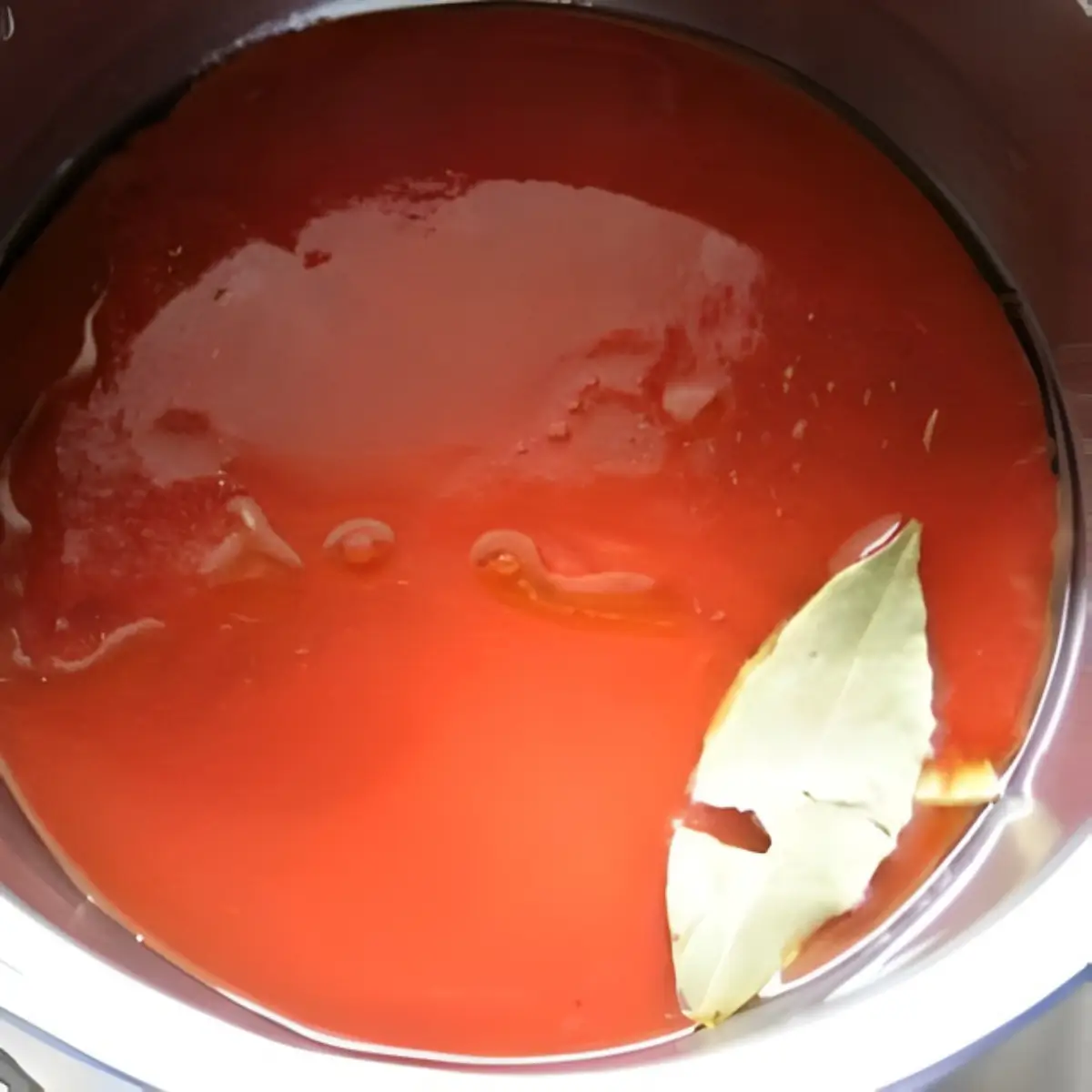 Tomato sauce simmering in a pot with a bay leaf on top.