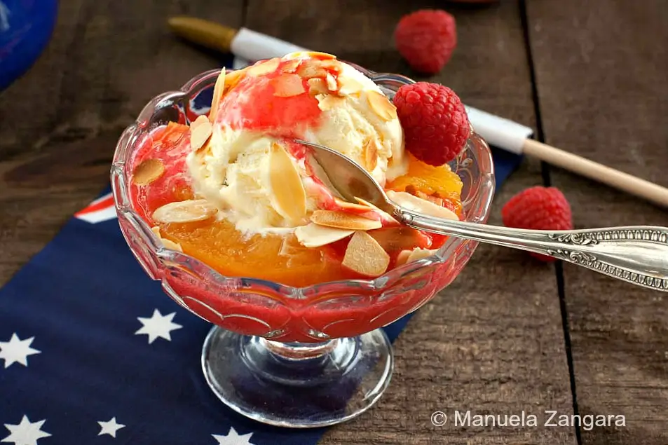 Close-up of Peach Melba with a spoon, showing peaches, ice cream, and raspberry coulis.