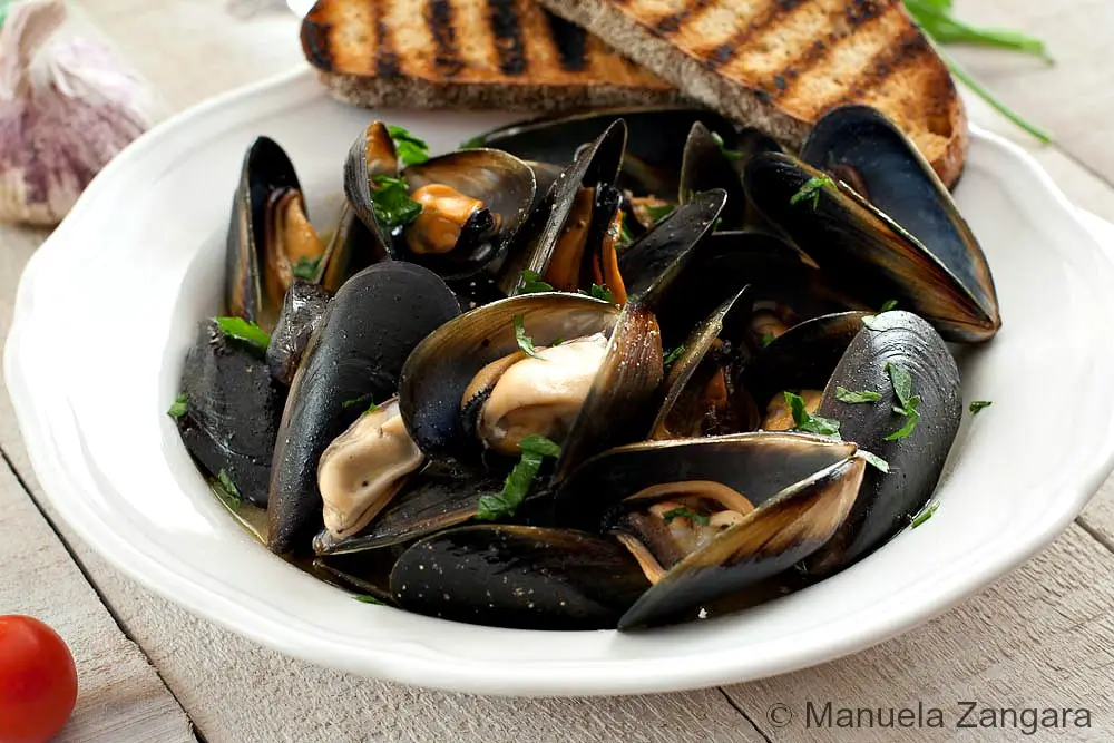 Steamed mussels in a bowl with parsley and olive oil.