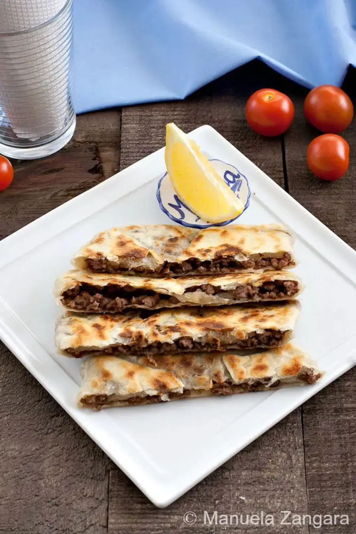 Sliced Lamb Gozleme on a plate with a lemon wedge and fresh tomatoes