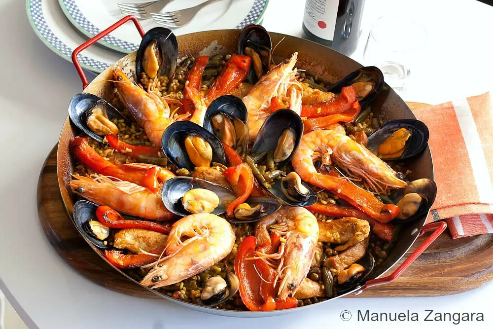 Paella Mixta with prawns, mussels, red peppers, and rice served in a pan.