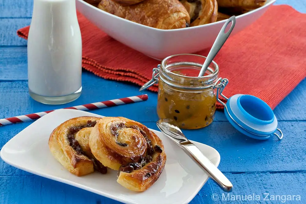 Close-up of two baked pain aux raisins on a white plate with jam nearby.