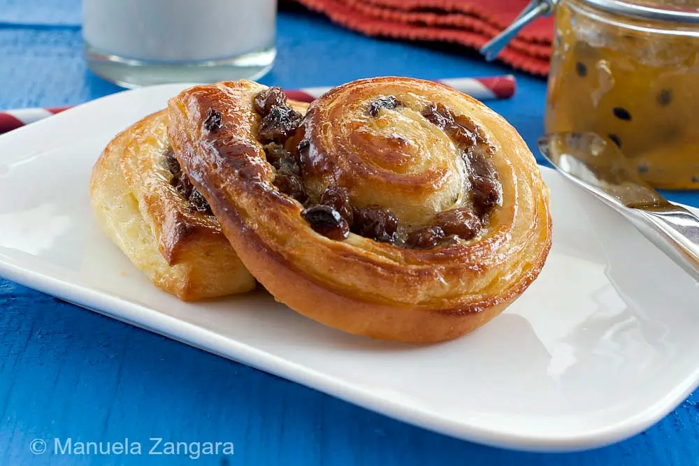 Close-up of two golden pain aux raisins on a white plate.