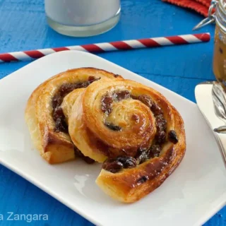 Freshly baked pain aux raisins served on a plate with milk and jam.