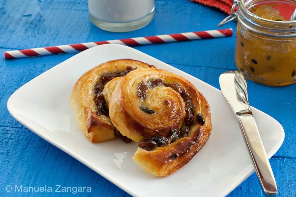 Freshly baked pain aux raisins served on a plate with milk and jam.