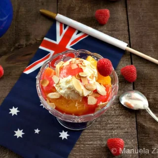 Peach Melba served in a glass bowl with vanilla ice cream, raspberry sauce, and toasted almonds.