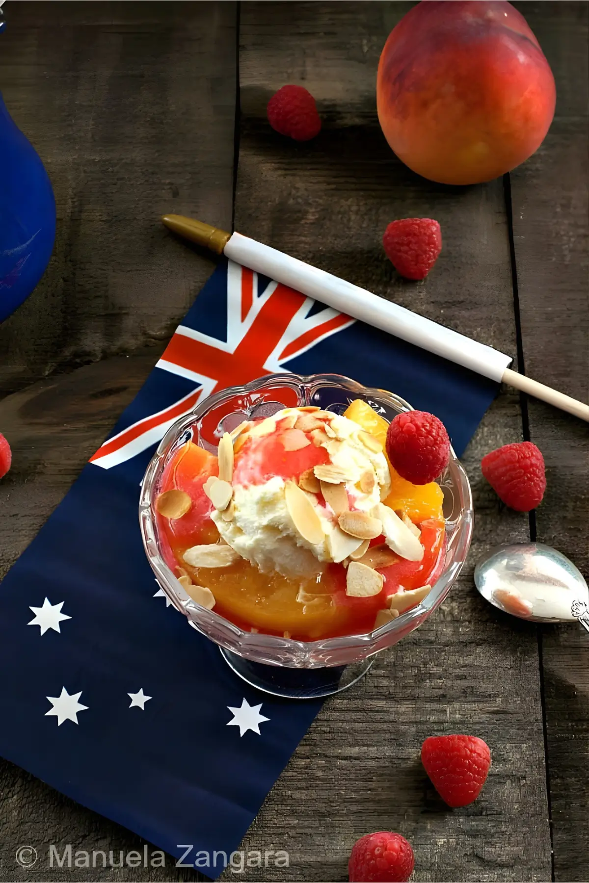 Peach Melba served in a glass bowl with vanilla ice cream, raspberry coulis, and toasted almonds.