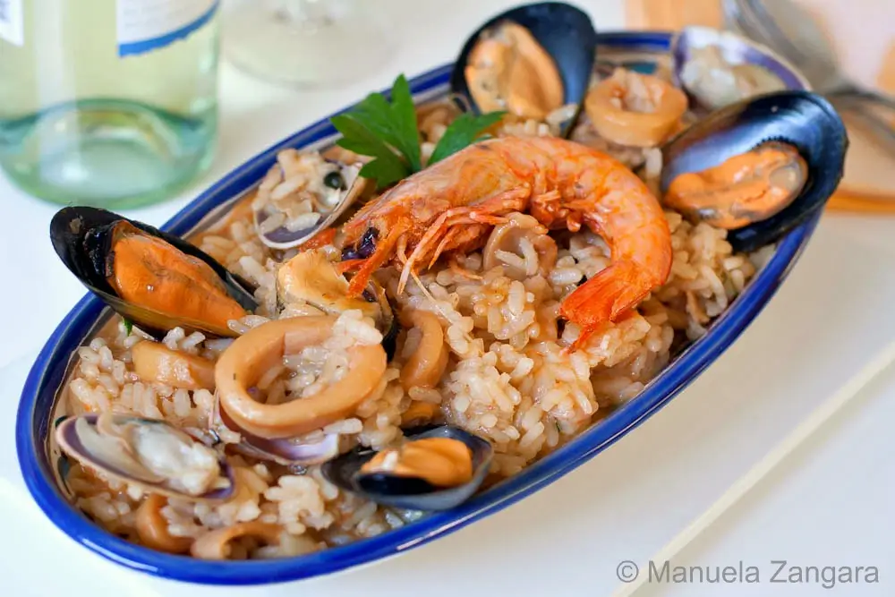 Risotto alla Marinara with mussels, clams, squid, and a prawn served in an oval dish, garnished with parsley.