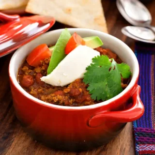Close-up of chili topped with sour cream, avocado, tomato, and coriander.