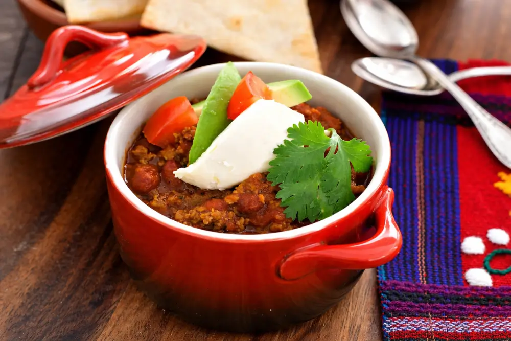 Close-up of chili topped with sour cream, avocado, tomato, and coriander.