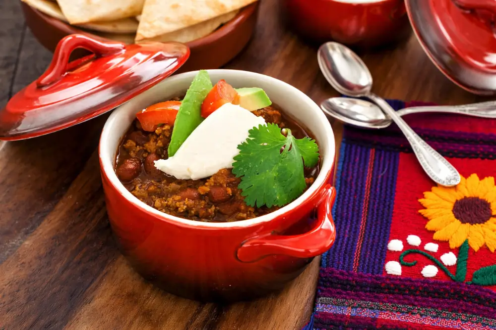 Chili con Carne with Beans served in a red pot with fresh toppings on a wooden board.