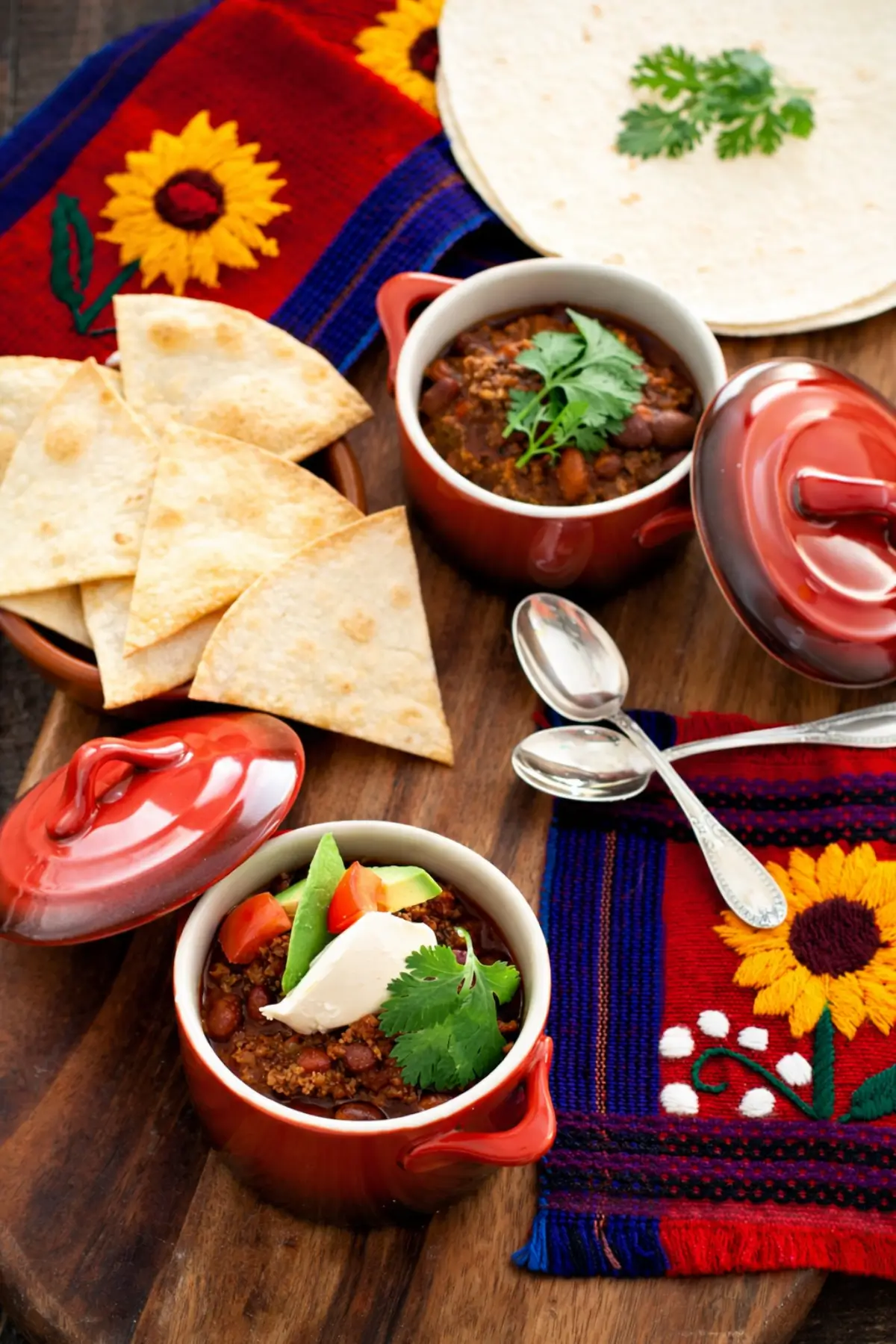 Bowl of chili served with tortilla chips, soft tortillas, and colourful cloth.