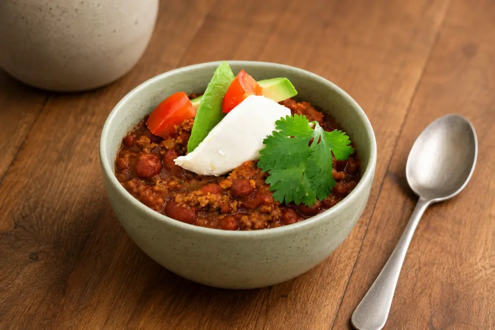 Bowl of beef and bean chilli topped with avocado, tomato, sour cream and fresh coriander.