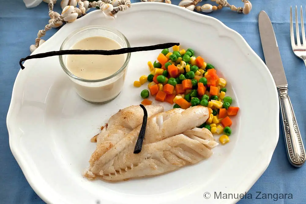 Fish Fillet with Tahitian Vanilla Sauce served with mixed vegetables and a small glass of sauce.