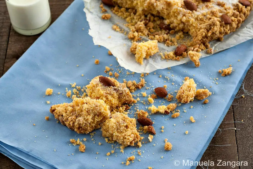 Crumbled pieces of Sbrisolona with whole almonds scattered on a blue cloth.