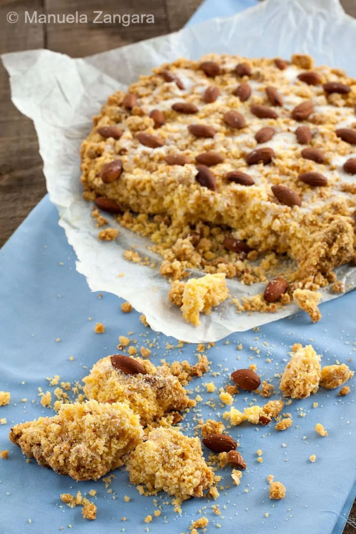Partially served Sbrisolona on baking paper with crumbs and almonds around it.