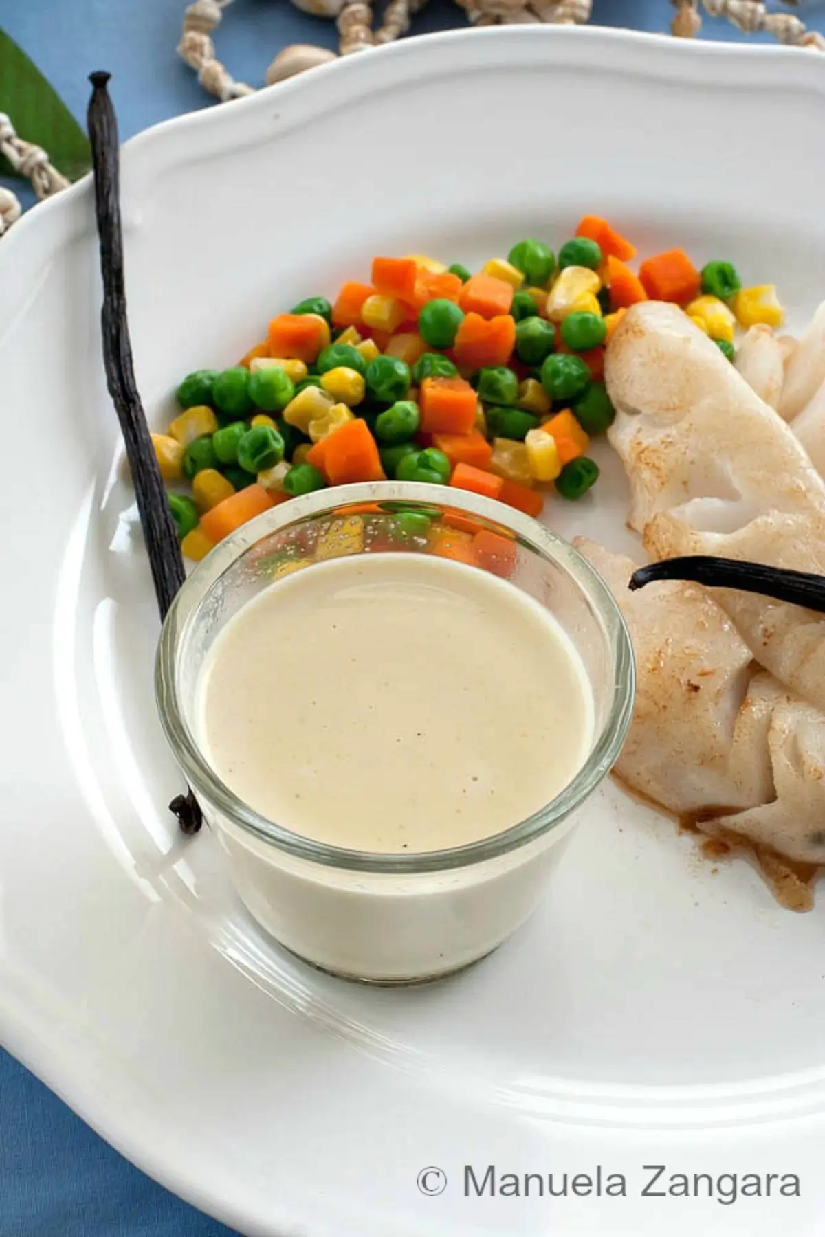 Close-up of vanilla sauce in a small glass beside mixed vegetables on the plate.
