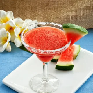 Watermelon margarita in a sugar-rimmed glass with fresh watermelon slices on the side.