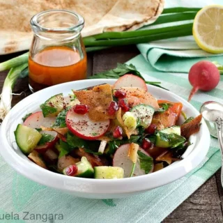 A fresh bowl of Fattoush salad with crispy khubz, cucumbers, radishes, pomegranate, and sumac dressing.