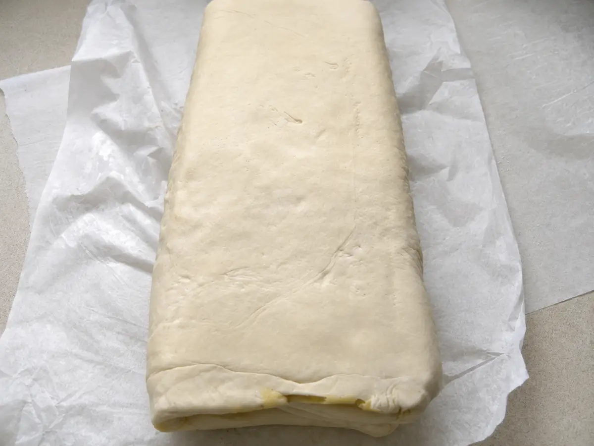 Folded puff pastry resting on baking paper with laminated layers visible along the edge.