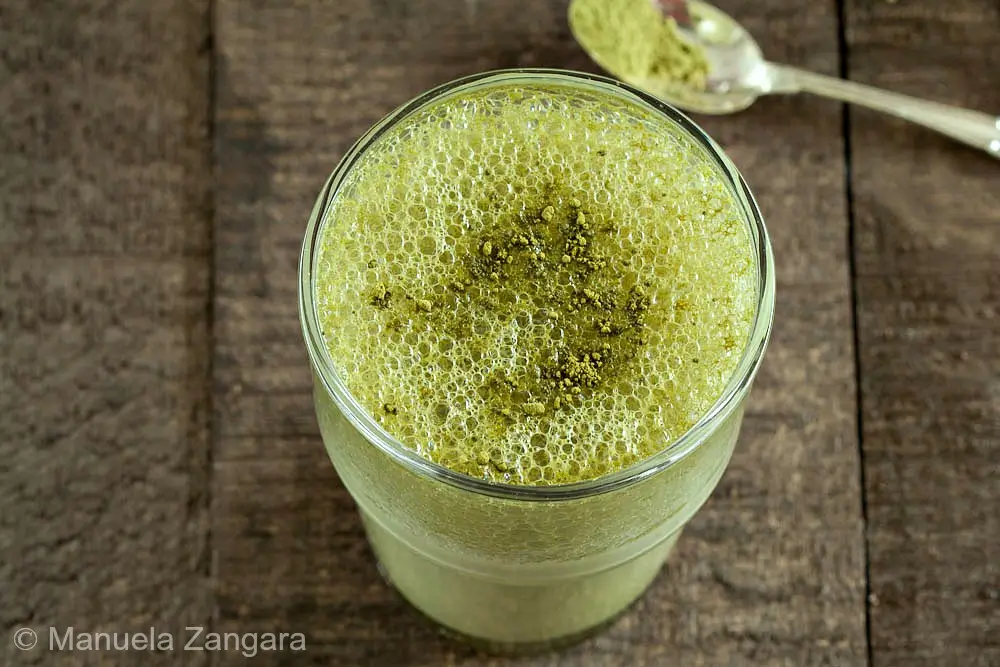 Close-up of frothy matcha milk with fine bubbles and dusted tea powder.
