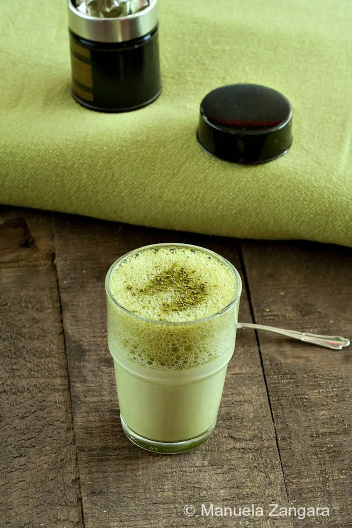 Green Tea Latte in a clear glass with creamy foam and matcha sprinkled on top.