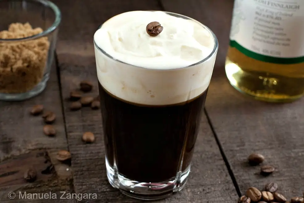 Irish Coffee topped with soft whipped cream on a wooden table.