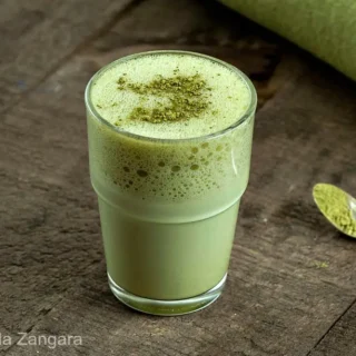 Glass of creamy matcha latte served on a rustic wooden table with spoon.
