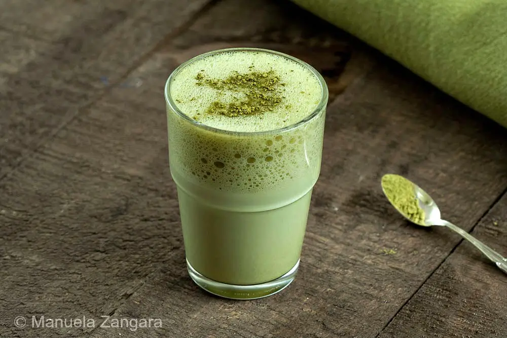 Glass of creamy matcha latte served on a rustic wooden table with spoon.