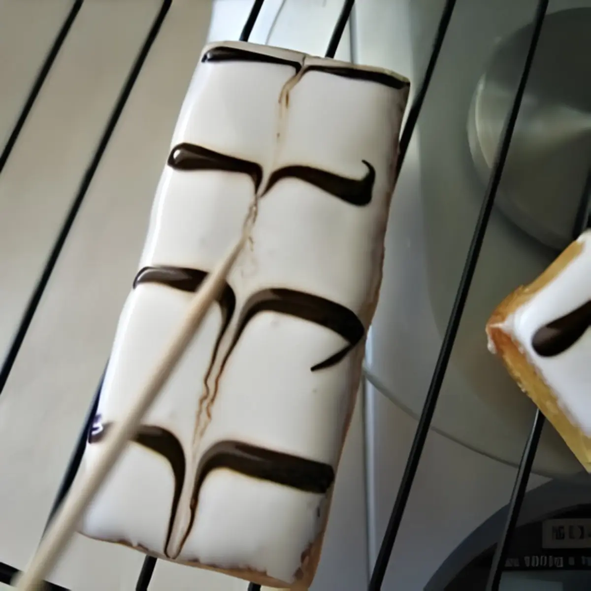 Iced mille-feuille with chocolate lines being pulled into a feather pattern using a toothpick.