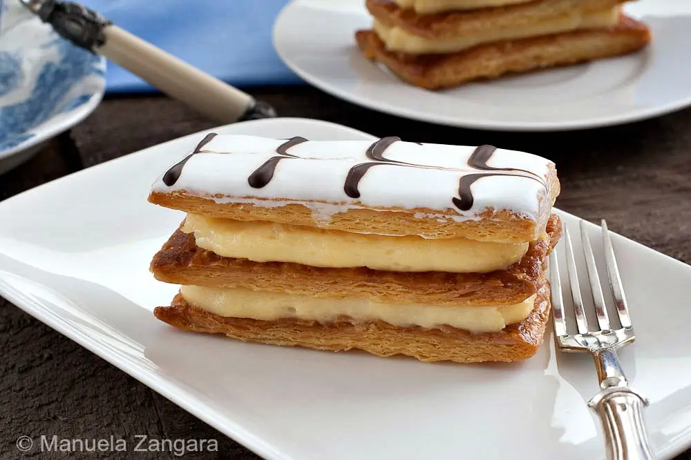 Finished mille-feuille with iced top and chocolate lines served on a white plate with a fork.