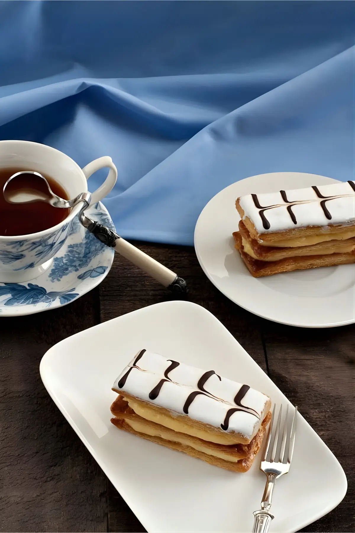 Mille-feuille slices on plates with a cup of tea on a wooden table.