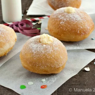 Sugar-dusted bombolone topped with crema pasticcera on parchment paper.