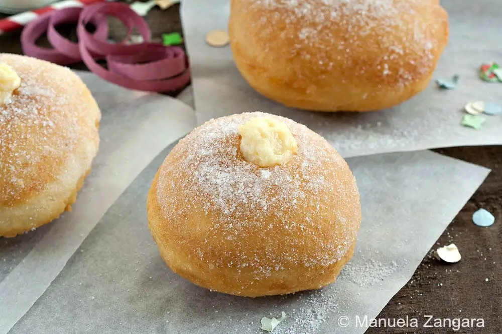Single sugar-dusted bombolone  all crema on parchment paper.