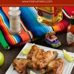 Grilled Margarita Chicken Wings on a white plate with lime wedges, coarse salt, tequila bottle.