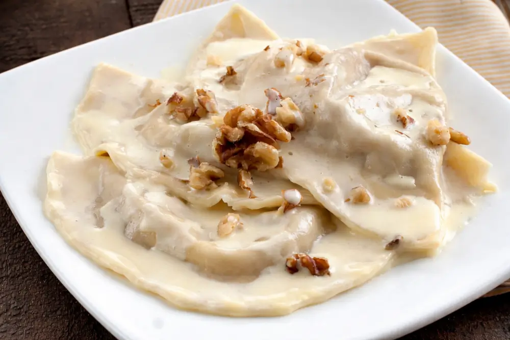 Close-up of half-moon stuffed pasta covered in Parmigiano fondue and walnuts.