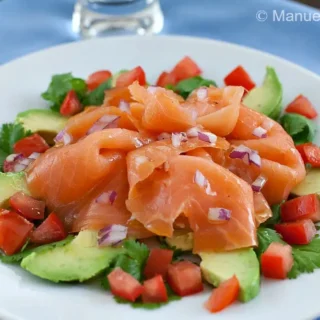 Close-up of smoked salmon and avocado salad on a white plate.