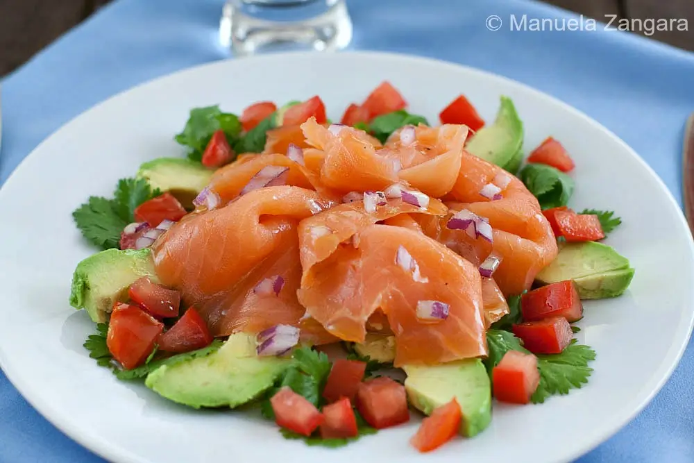 Close-up of smoked salmon and avocado salad on a white plate.