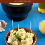 Creamy Patatas Alioli served in a bowl with aioli and garlic cloves nearby.