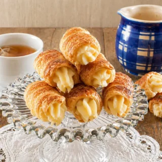 Golden puff pastry cannoncini served with hot tea and a blue ceramic coffee pot.